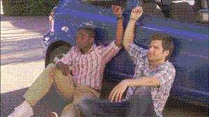 Shawn and Gus from the show Psych sitting down handcuffed to a car.
